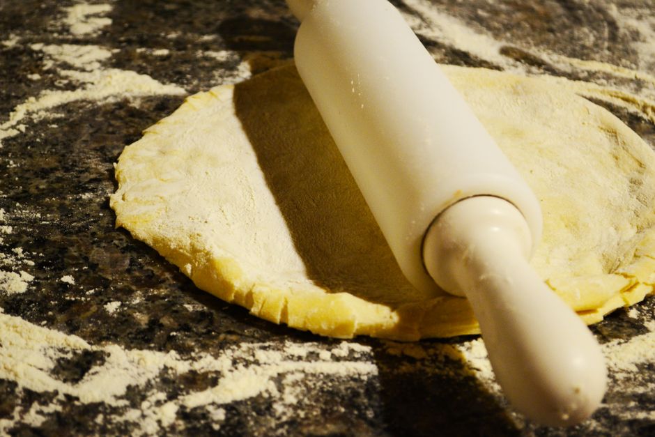 A close-up view of dough being prepared with a rolling pin on a flour-dusted surface.